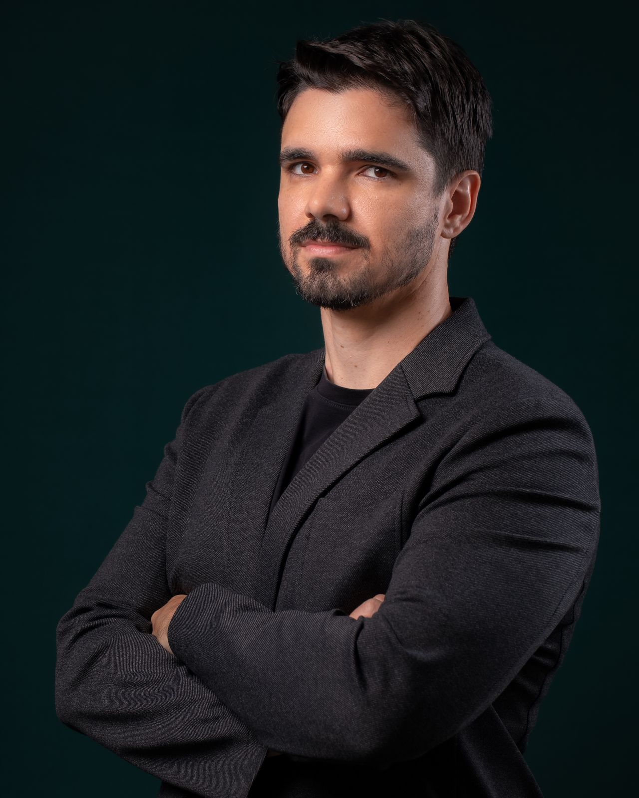 Retrato de Maycon Gabry, de braços cruzados, em fundo verde escuro